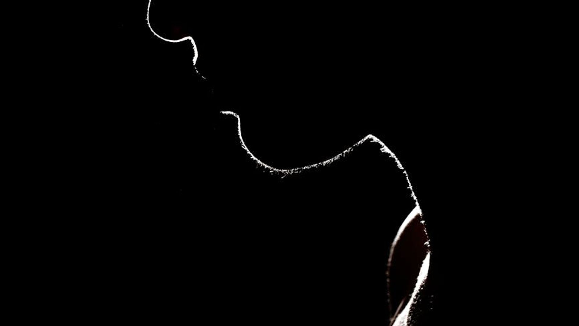 Silhouette of a person in a dynamic stretching pose against a dark, minimalist background.